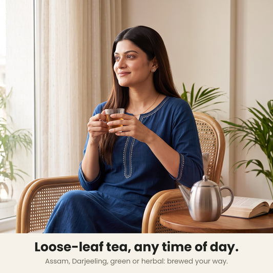 InstaCuppa steel tea pot — woman sipping loose-leaf tea in a cane chair, the pot on a side table beside her