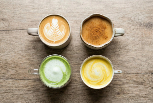 Four latte variations cafe chai matcha turmeric on wooden surface