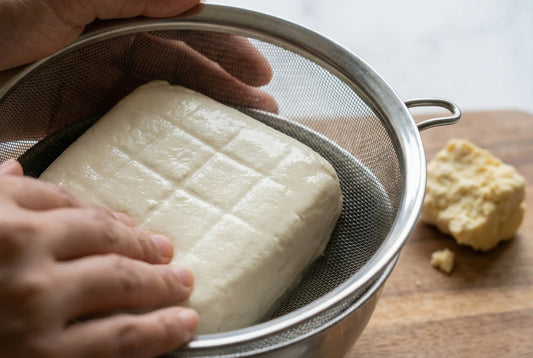 Soft paneer being pressed in strainer with even pressure