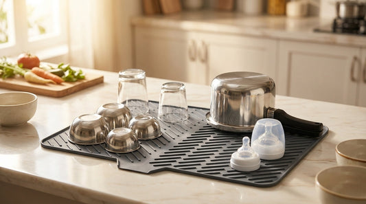 Silicone dish drying mat on an Indian kitchen counter with steel katoris, glasses, a pressure cooker and baby bottle parts drying on it