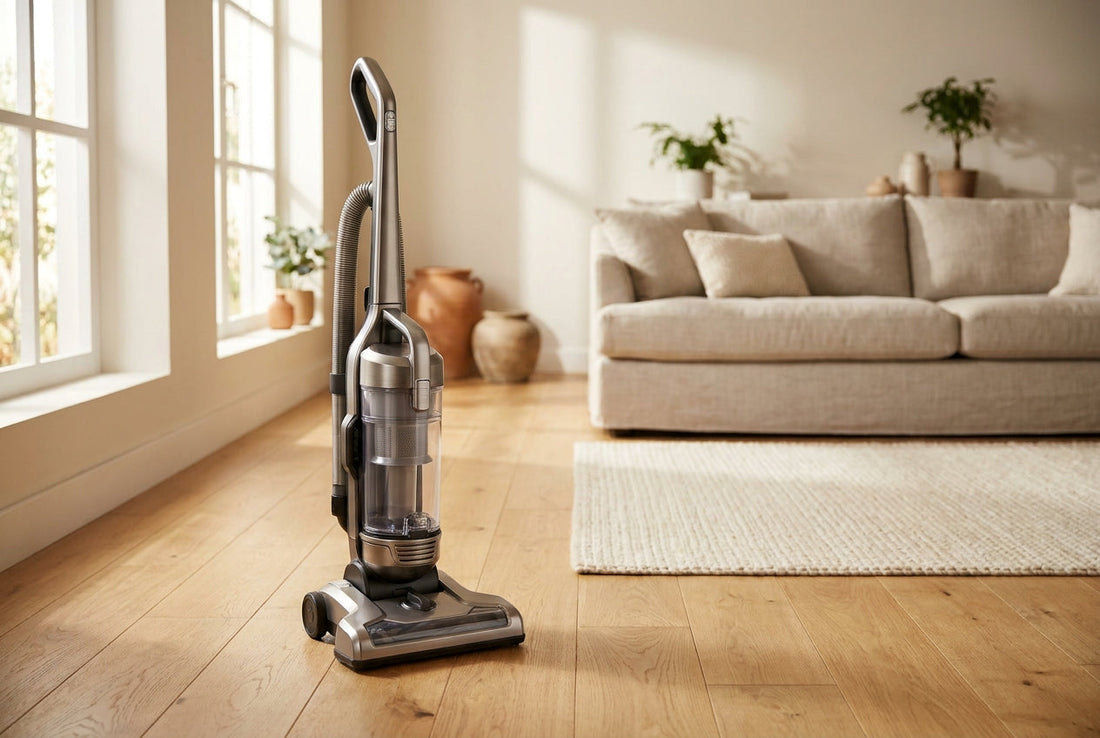 Upright bagless vacuum cleaner on a wooden floor in a bright living room with sofa and rug