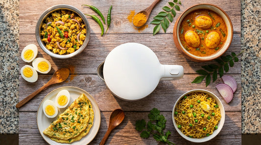 Top-down view of egg dishes around a multicook kettle - hard boiled eggs, egg bhurji, omelette, egg curry, and egg maggi on a wooden table with Indian spices
