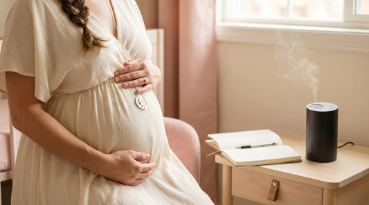 Pregnant woman in cream dress cradling belly with aroma diffuser on side table