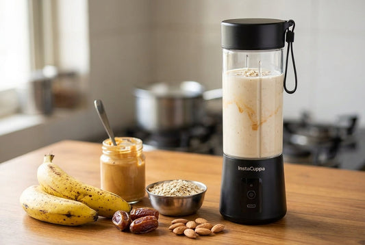 Banana shake for weight gain - the black InstaCuppa portable blender filled with a thick banana peanut shake beside ripe bananas, a jar of peanut butter, a bowl of oats, dates and almonds on a wooden table