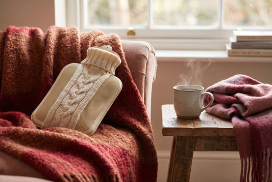 Best hot water bag in India 2026 — ribbed rubber hot water bottle in a knit cover on a cozy chair with a warm throw and tea