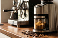 Burr coffee grinder with fresh ground coffee and espresso machine in background