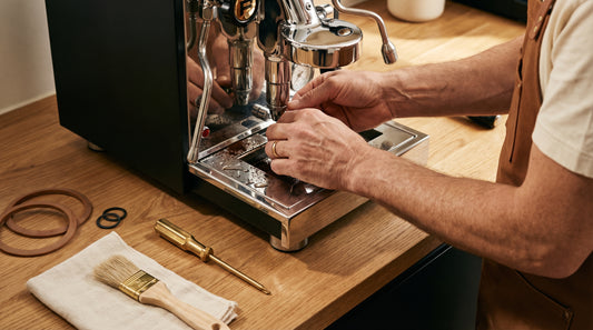 Hands troubleshooting espresso machine with tools and cleaning supplies on counter