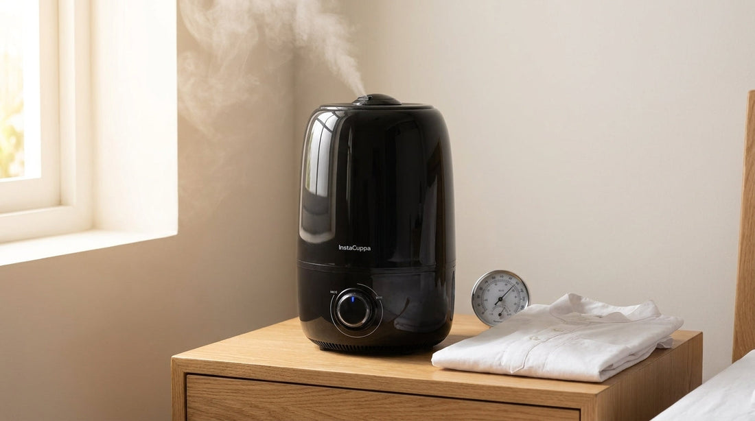 InstaCuppa 4 litre ultrasonic cool mist humidifier in glossy black on an oak bedside table in a bright Indian bedroom, mist rising from the nozzle, with a small analogue hygrometer and a folded white kurta beside it