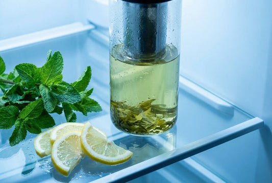 Glass tea infuser bottle with pale green cold-brewed tea on a refrigerator shelf