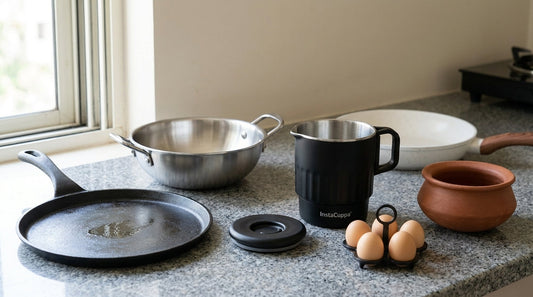 Non-stick pan alternatives on a granite Indian kitchen counter: a seasoned cast iron tawa, a triply stainless steel kadai, the InstaCuppa stainless steel multicook kettle with its lid and egg tray, a terracotta clay handi and a ceramic-coated frying pan