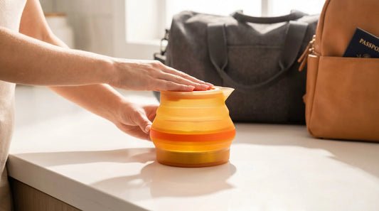 Hands folding a collapsible silicone kettle with travel bag nearby showing compact portability