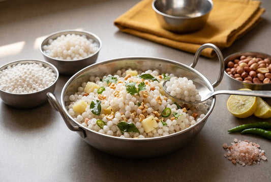 Sabudana khichdi in a steel kadhai with separate glossy pearls, potato, peanuts and curry leaves, beside bowls of dry and soaked sabudana, peanuts, lemon and rock salt