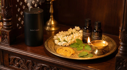 Sandalwood and jasmine essential oils with brass puja thali, mogra flowers, tulsi leaves, ghee diya, and InstaCuppa aroma diffuser on wooden mandir shelf