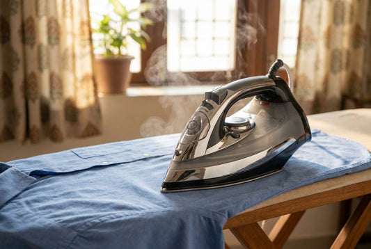 Steam iron gliding over a crisp blue cotton shirt on an ironing board with light steam