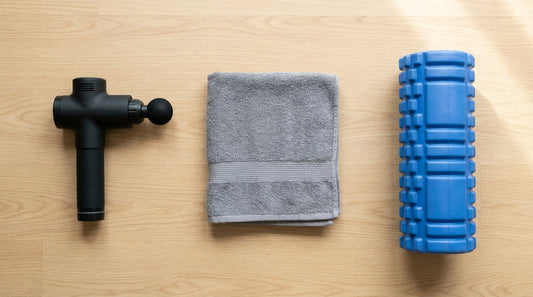 Massage gun and blue foam roller side by side with a towel on a wooden floor