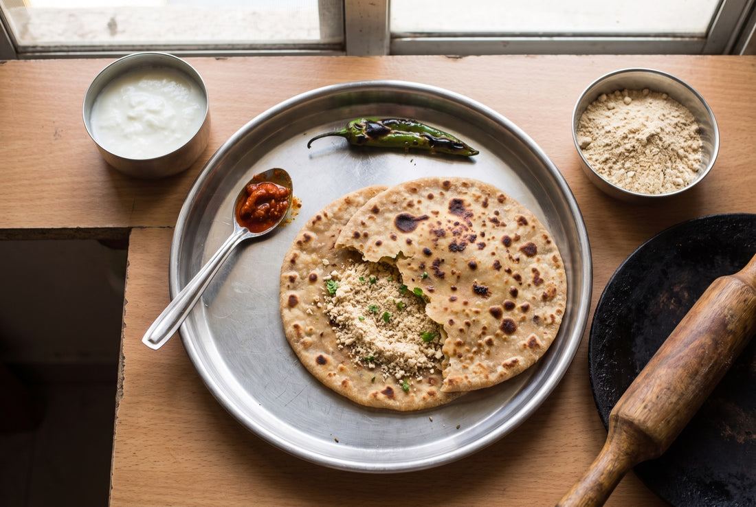 InstaCuppa sattu paratha recipe: two whole-wheat sattu parathas on a steel plate, one torn open to show the dry, crumbly sattu filling, with curd, mango pickle, a roasted green chilli and a bowl of sattu
