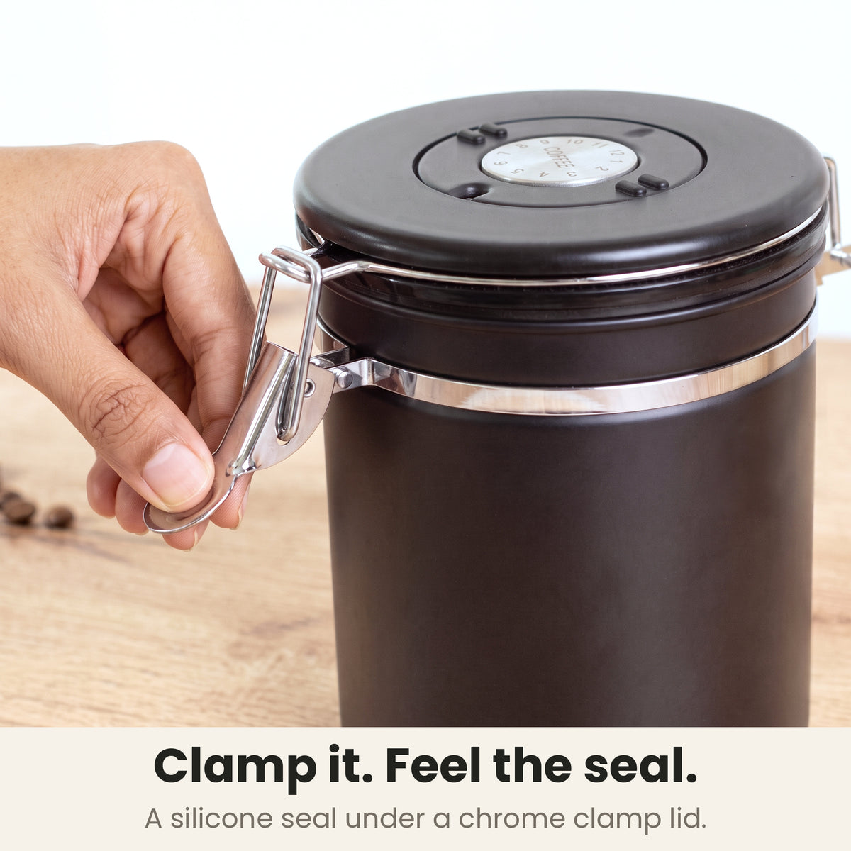 Airtight coffee container - Black - chrome clamp lid closing on a silicone seal, a hand pressing the clamp shut