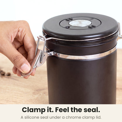 Airtight coffee container - Black - chrome clamp lid closing on a silicone seal, a hand pressing the clamp shut