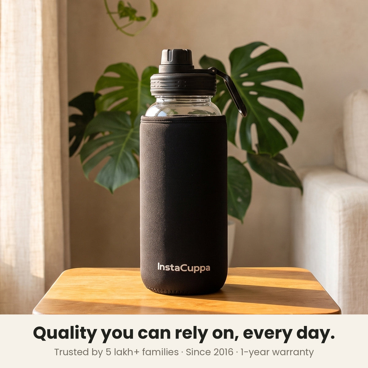 InstaCuppa Borosilicate Glass Water Bottle 1 Litre - Black - trusted by 5 lakh+ families since 2016, 1-year warranty: the sleeved bottle on a table by the window