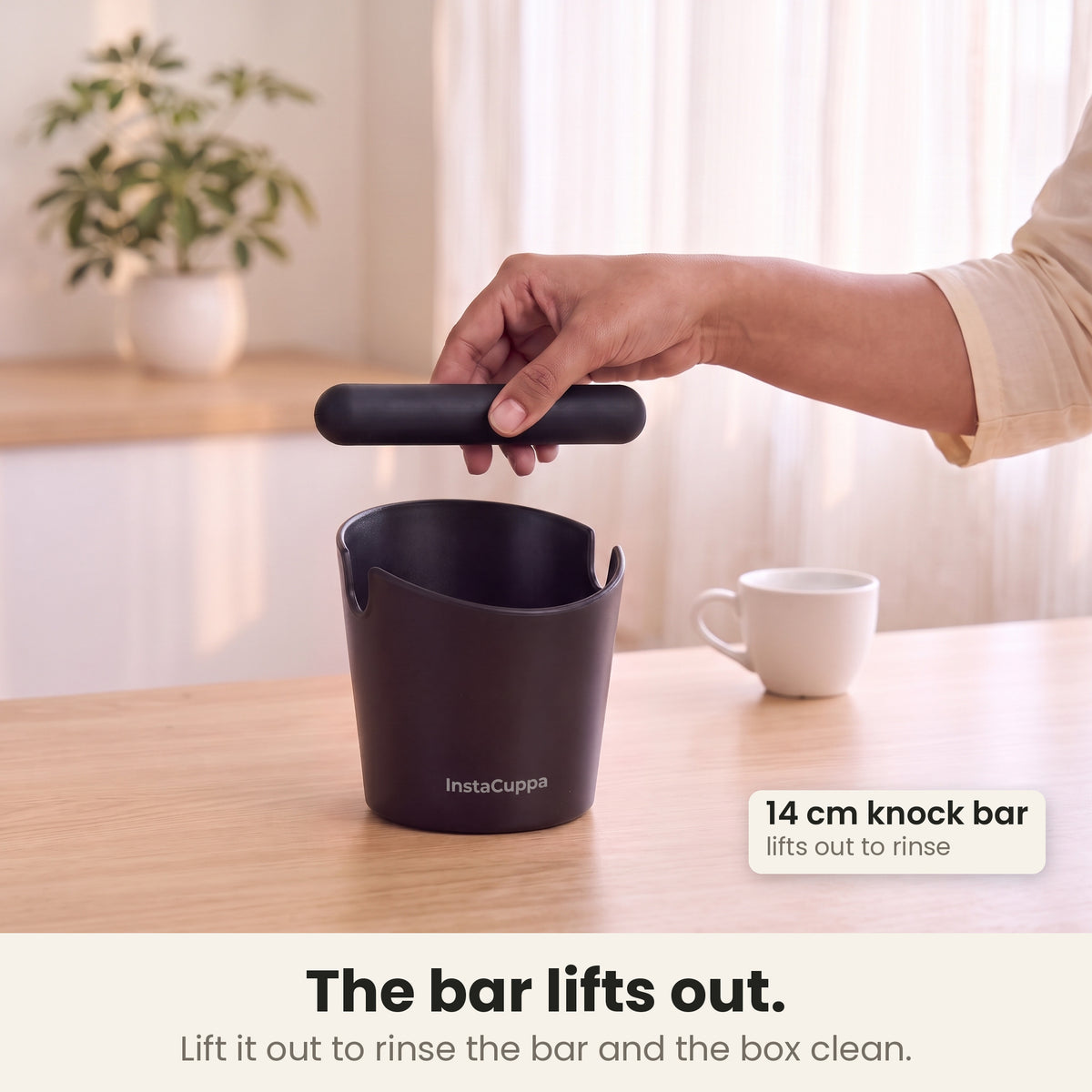 Coffee knock box with the 14 cm knock bar lifted out of its notches for rinsing, in a bright kitchen