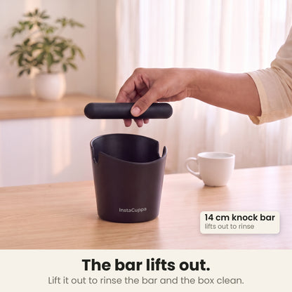 Coffee knock box with the 14 cm knock bar lifted out of its notches for rinsing, in a bright kitchen