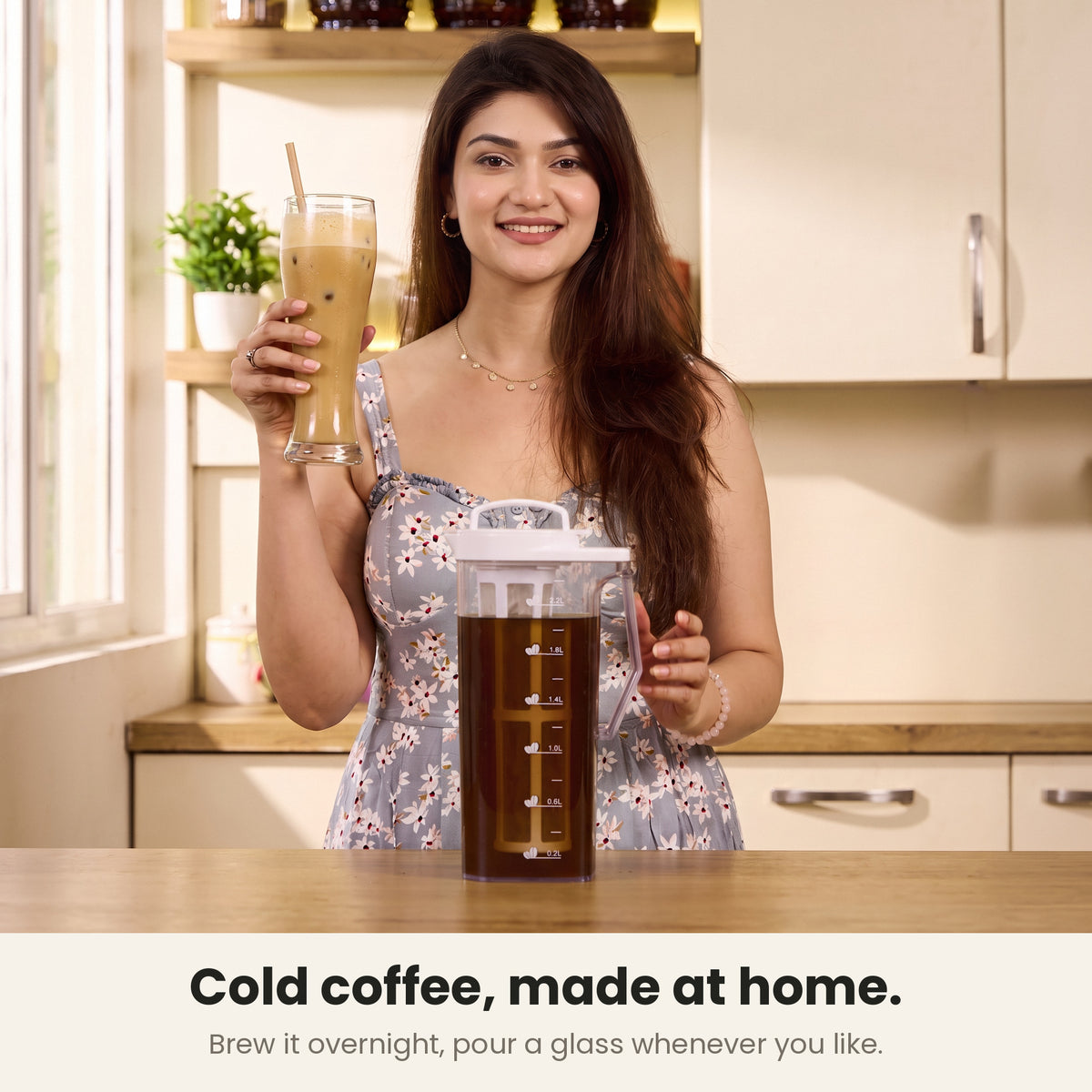 InstaCuppa cold brew coffee maker — woman holding a tall glass of Indian cafe-style cold coffee at her kitchen counter beside the jug of overnight brew