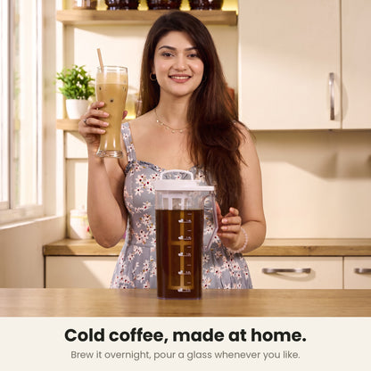 InstaCuppa cold brew coffee maker — woman holding a tall glass of Indian cafe-style cold coffee at her kitchen counter beside the jug of overnight brew
