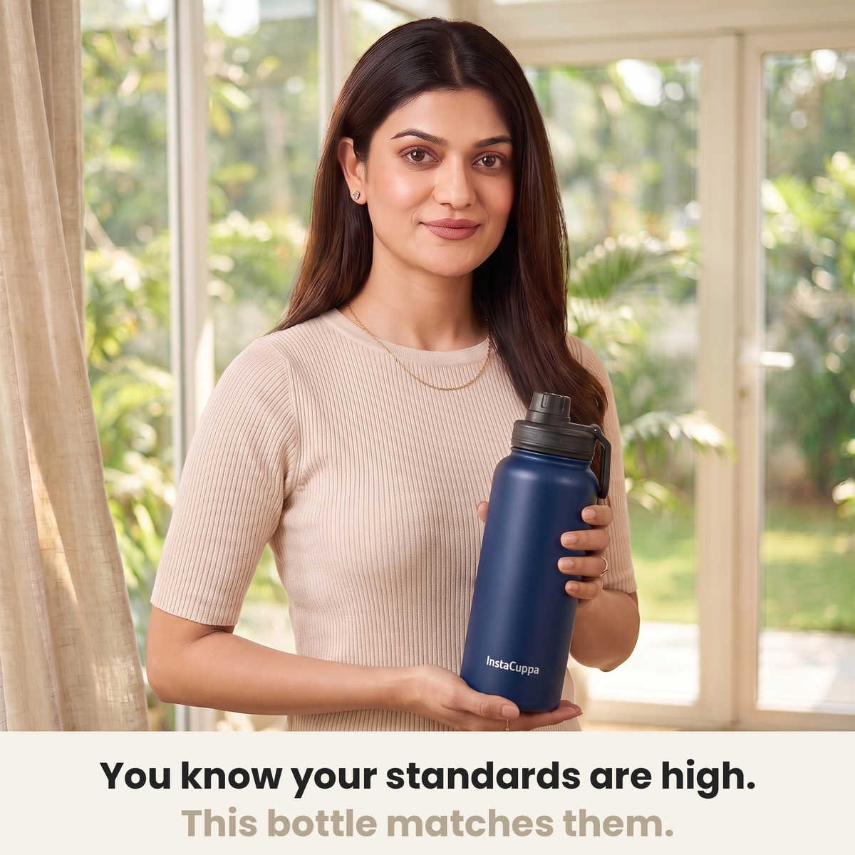 InstaCuppa Insulated Water Bottle 1L (1000 ml) - Navy Blue - woman in a cream ribbed knit top holding the bottle in a sunlit room, caption: you know your standards are high, this bottle matches them