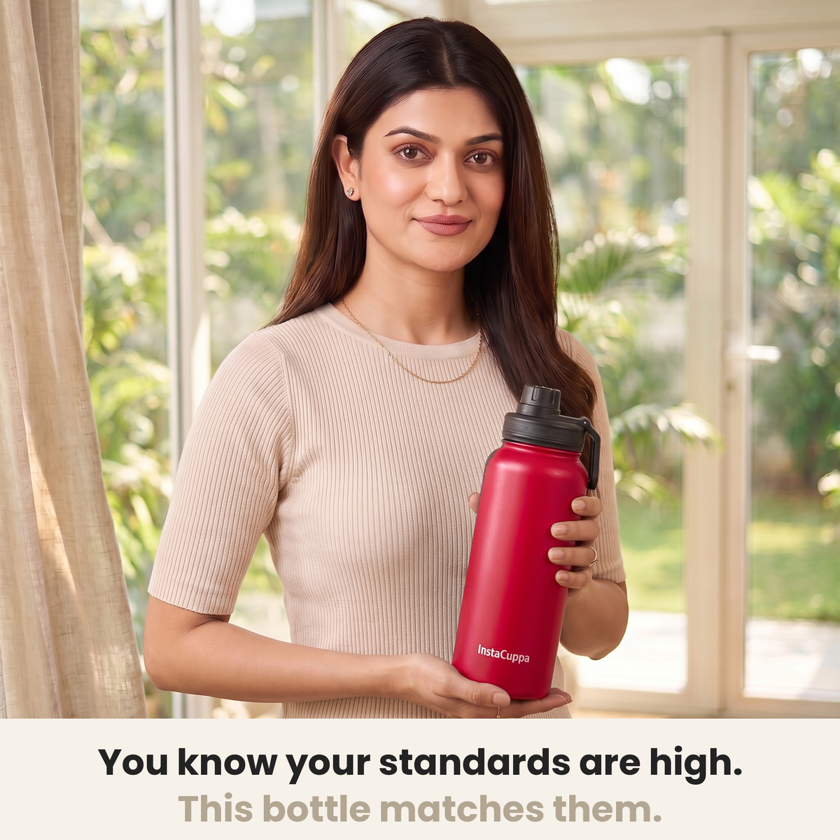 InstaCuppa Insulated Water Bottle 1L (1000 ml) - Red - woman in a cream ribbed knit top holding the bottle in a sunlit room, caption: you know your standards are high, this bottle matches them