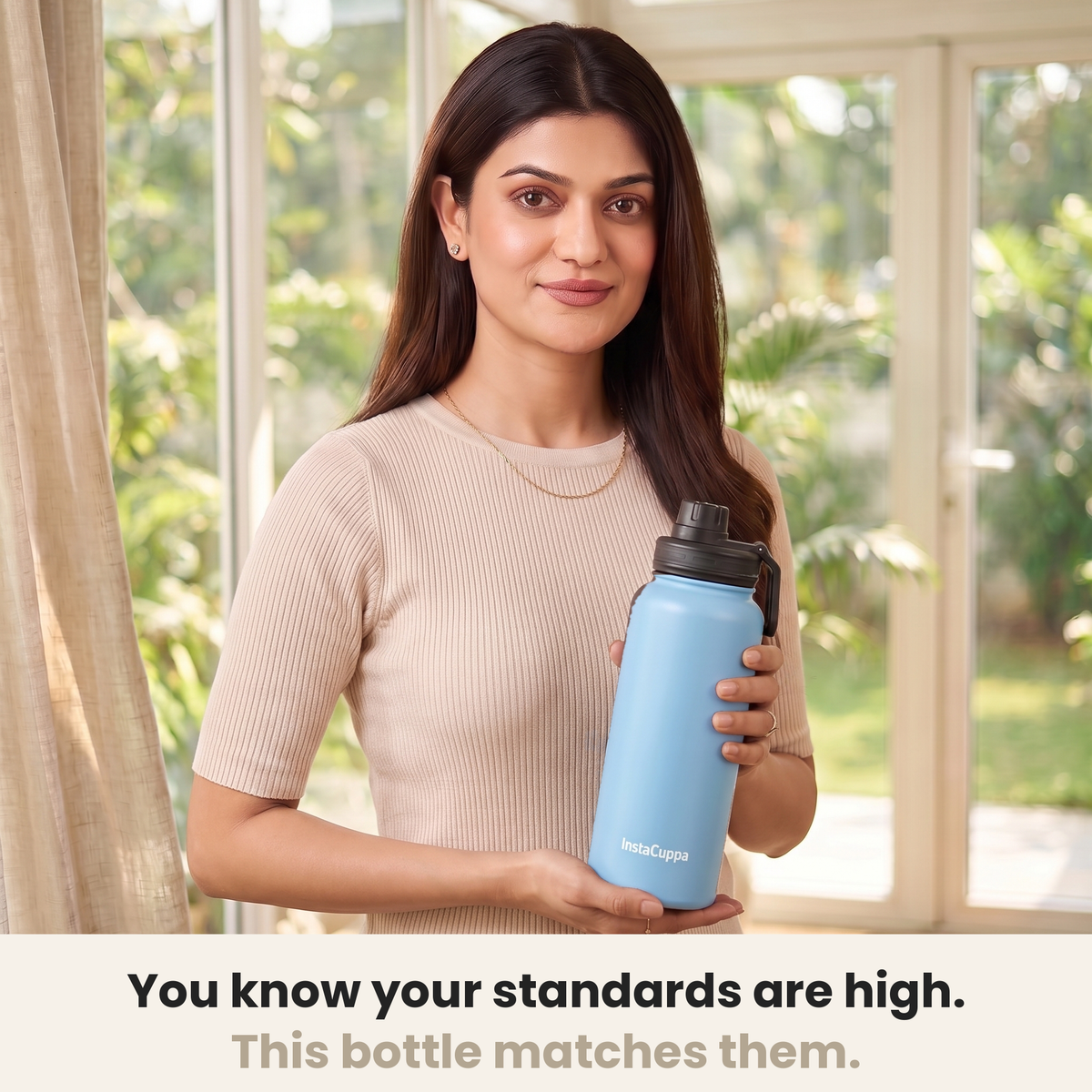 InstaCuppa Insulated Water Bottle 1L (1000 ml) - Sky Blue - woman in a cream ribbed knit top holding the bottle in a sunlit room, caption: you know your standards are high, this bottle matches them