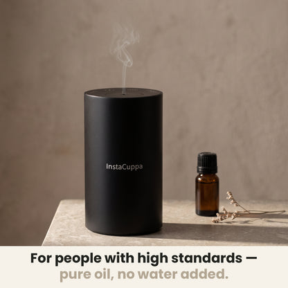 InstaCuppa Rechargeable Aroma Oil Diffuser - for people with high standards, pure oil, no water added: the diffuser misting on a stone side table beside an amber essential oil bottle