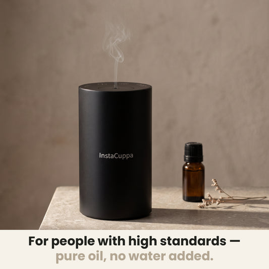 InstaCuppa Rechargeable Aroma Oil Diffuser - for people with high standards, pure oil, no water added: the diffuser misting on a stone side table beside an amber essential oil bottle