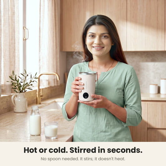 InstaCuppa Self Stirring Mug 300 ml - Light Beige - hot or cold, stirred in seconds: a woman in her kitchen holding the mug, chilled milk on the counter; no spoon needed, it stirs and doesn't heat