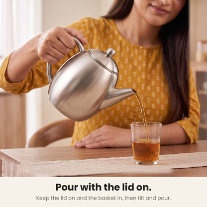 InstaCuppa steel tea pot — woman pouring by its steel loop handle with the lid on and the basket in