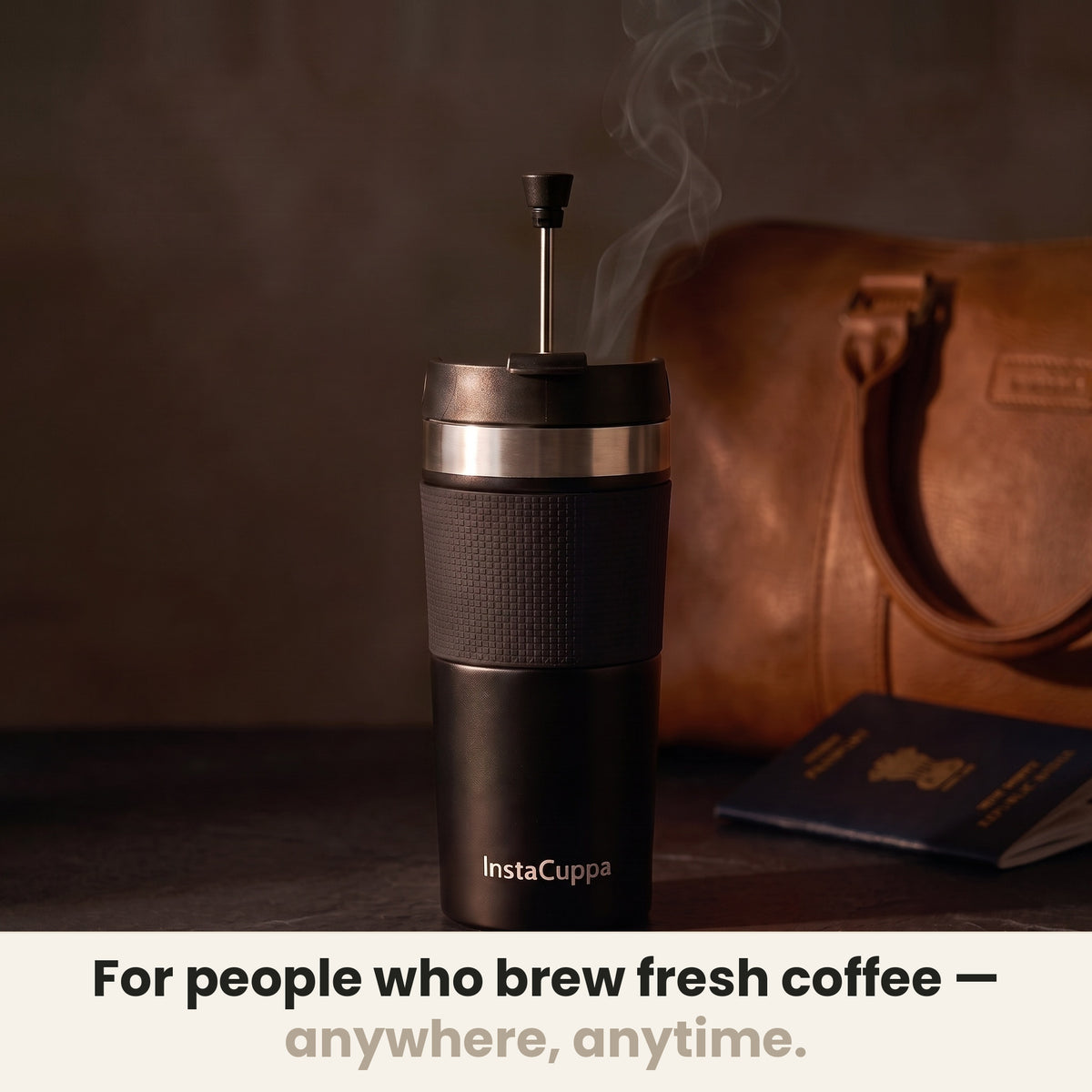 InstaCuppa Travel French Press Mug 400 ml - Black - for people who brew fresh coffee anywhere, anytime: the press with its plunger up beside a leather bag and a passport