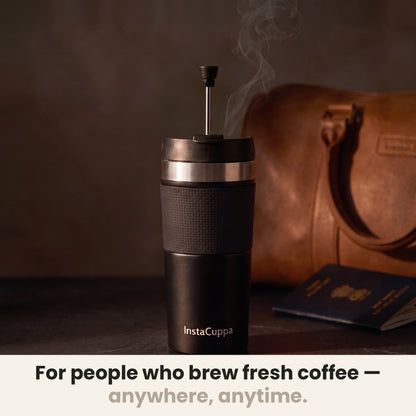 InstaCuppa Travel French Press Mug 400 ml - Black - for people who brew fresh coffee anywhere, anytime: the press with its plunger up beside a leather bag and a passport