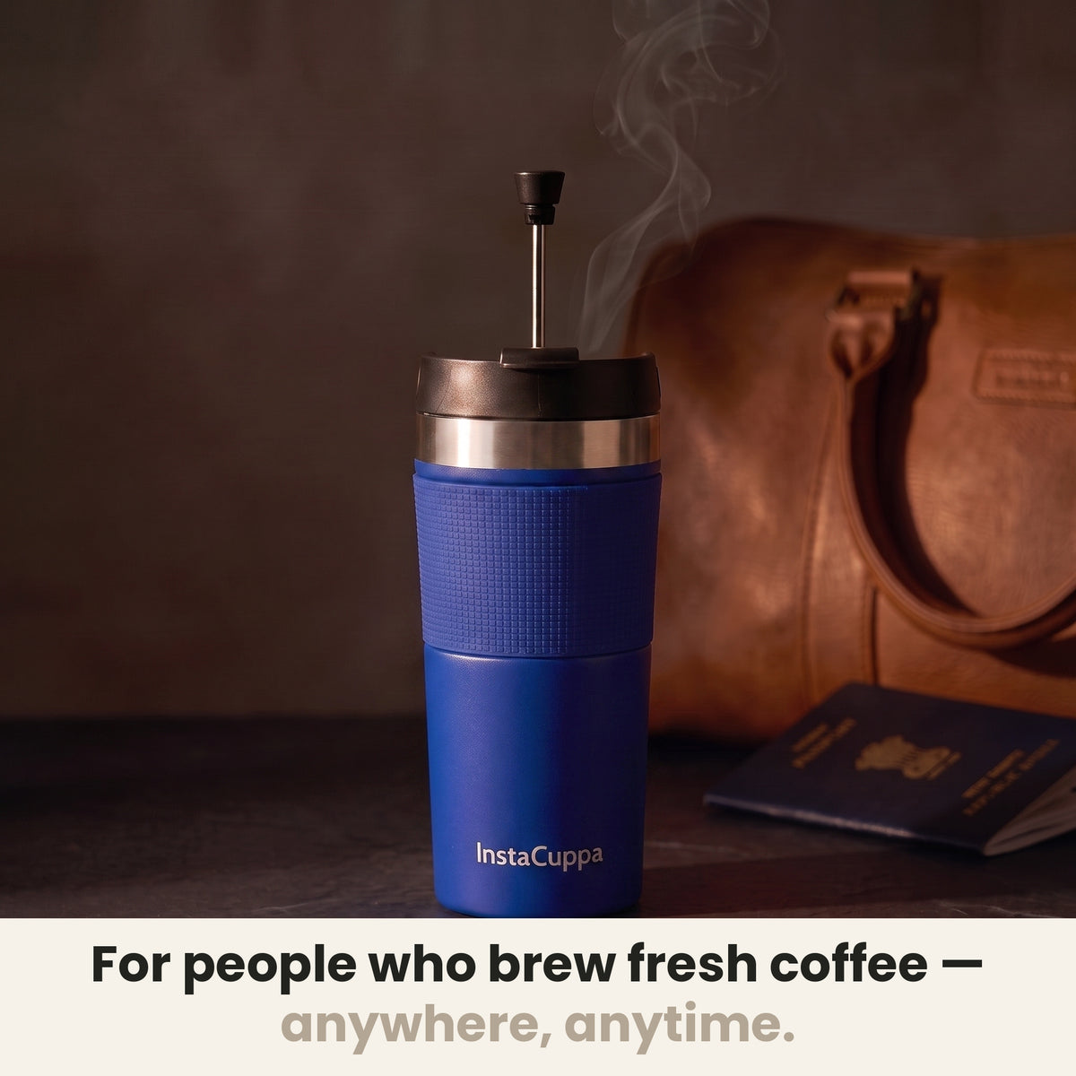 InstaCuppa Travel French Press Mug 400 ml - Navy Blue - for people who brew fresh coffee anywhere, anytime: the press with its plunger up beside a leather bag and a passport
